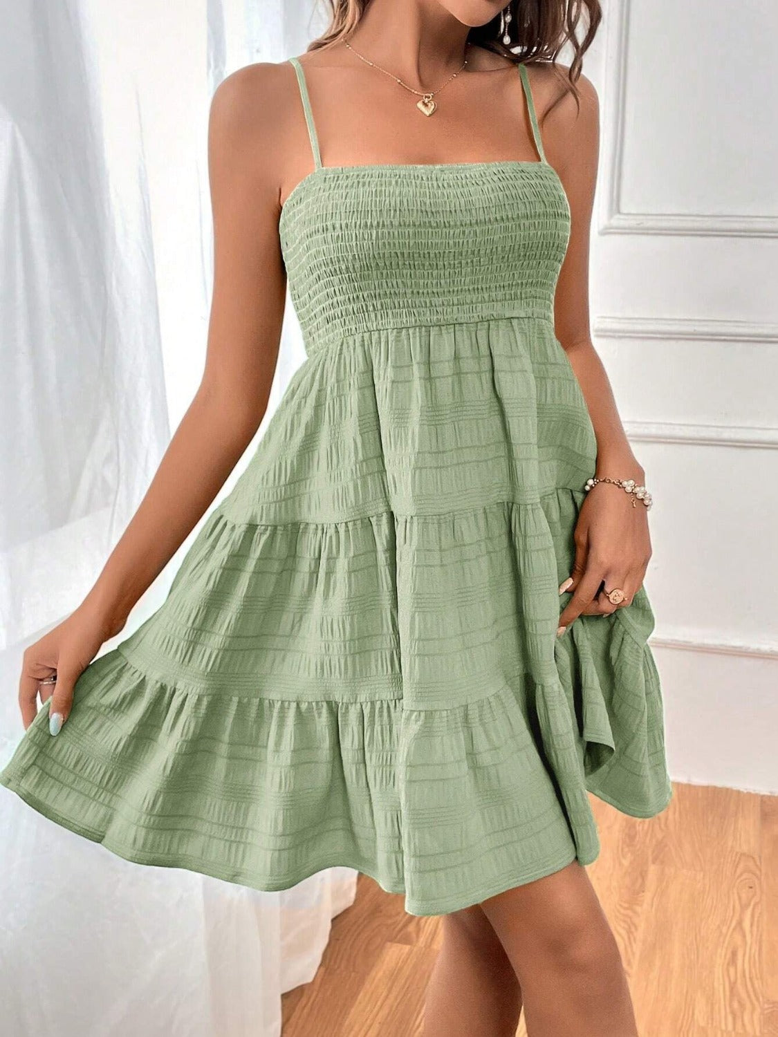 Chic green tiered sundress featuring slim straps and a shirred bodice, perfect for a summer day. Accessorized with heart pendant and subtle jewelry.