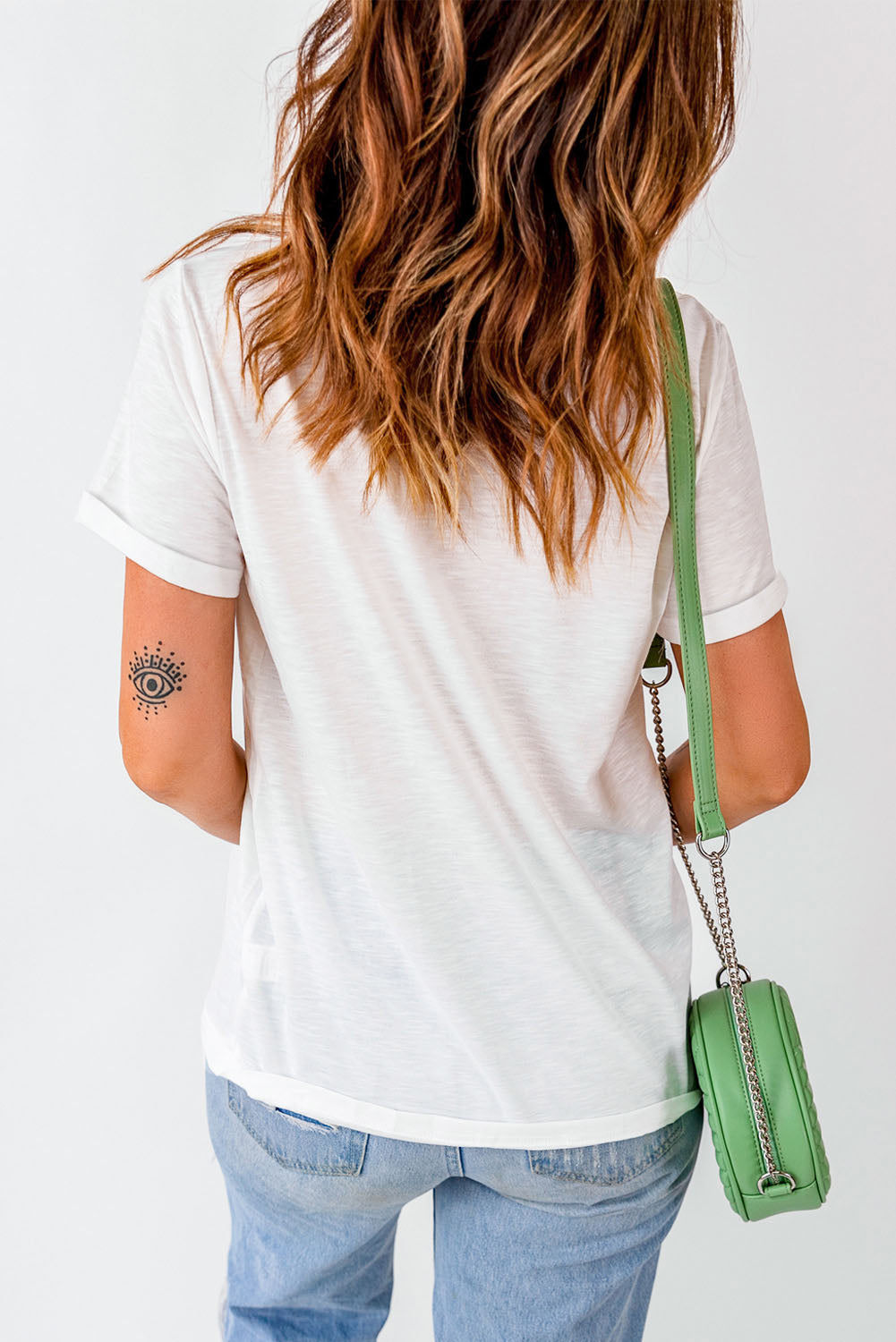 Casual summer fashion with a woman in a white tee and blue jeans, flaunting a trendy arm tattoo and a chic green shoulder bag. Perfect for a relaxed yet stylish look!