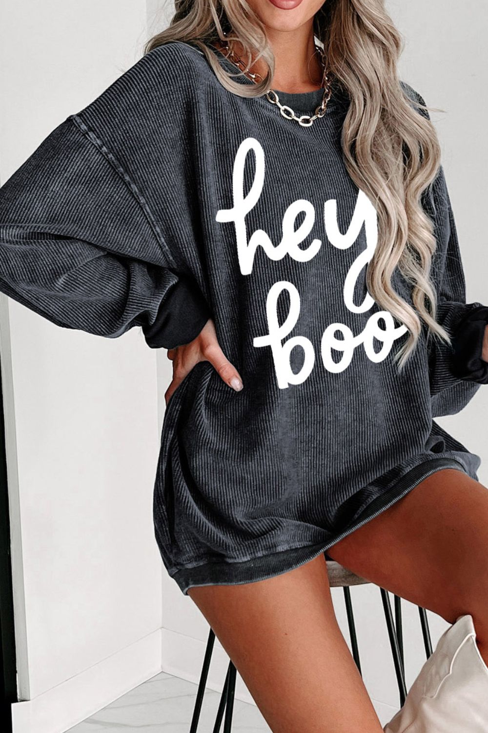 Woman in a stylish oversized gray sweatshirt with "hey boo" print, paired with chic accessories, embodying a casual yet trendy autumn vibe. Perfect for cozy fashion statements.