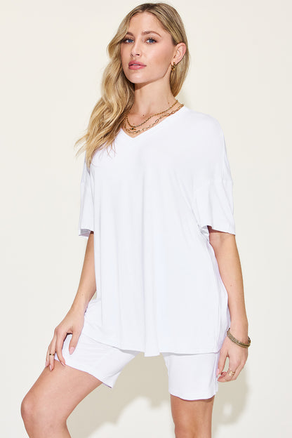 Elegant woman in a chic white tee and shorts ensemble accessorized with layered necklaces and stylish bracelets, exuding casual sophistication.