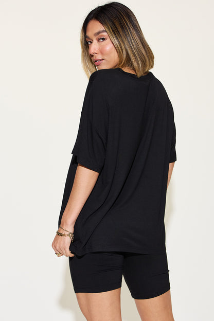 Chic woman in a casual black oversized tee and fitted shorts, turning her gaze over the shoulder with understated elegance. Shop this versatile summer look! #SummerFashion #CasualStyle #WomensWear