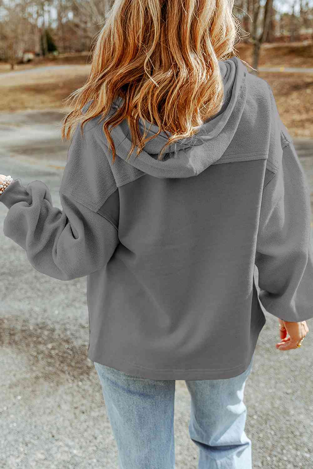 Back view of a woman in a casual gray hoodie and blue jeans, showcasing laid-back streetwear style with tousled hair, against a soft natural backdrop. Perfect for cozy fashion looks.