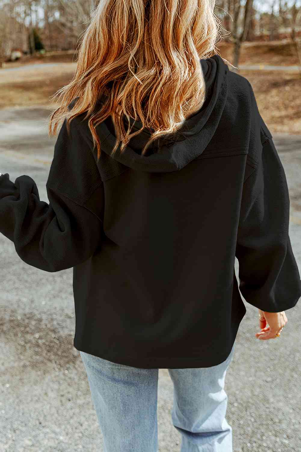 Rear view of a woman in a casual black hoodie and blue jeans walking outdoors, with a focus on trendy autumn fashion and natural wavy hair.