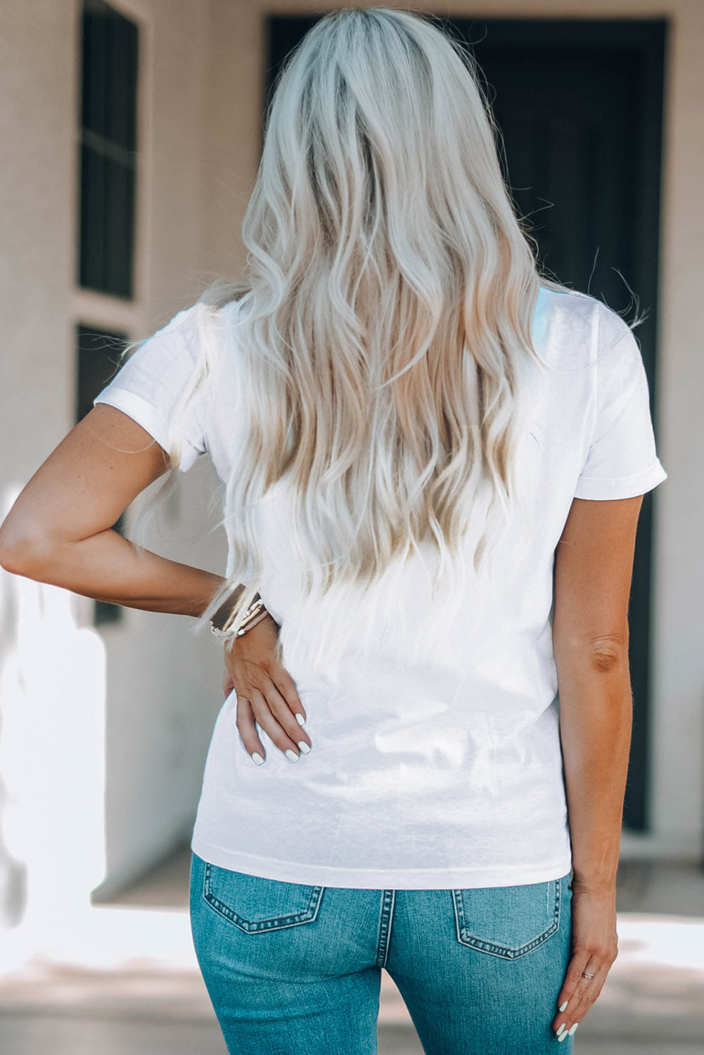 Blonde woman in white tee and blue jeans standing with back to camera, showcasing a casual chic style. Ideal for fashion and lifestyle content.