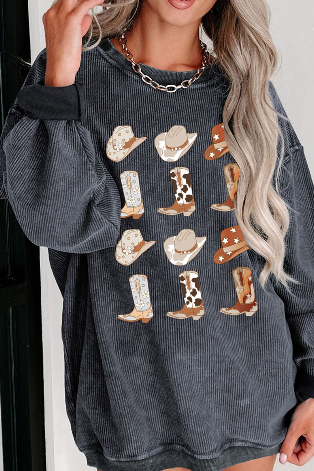 Stylish woman in a western-themed, long-sleeved corduroy shirt adorned with cowboy boots and hat patches, paired with a chunky chain necklace. Perfect for a casual, country-inspired look.