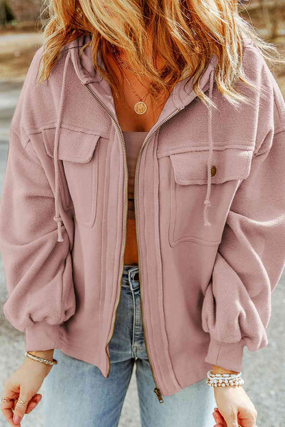 Woman in a stylish mauve zip-up hoodie and denim jeans accessorized with layered necklaces and a beaded bracelet, embodying casual chic fashion.