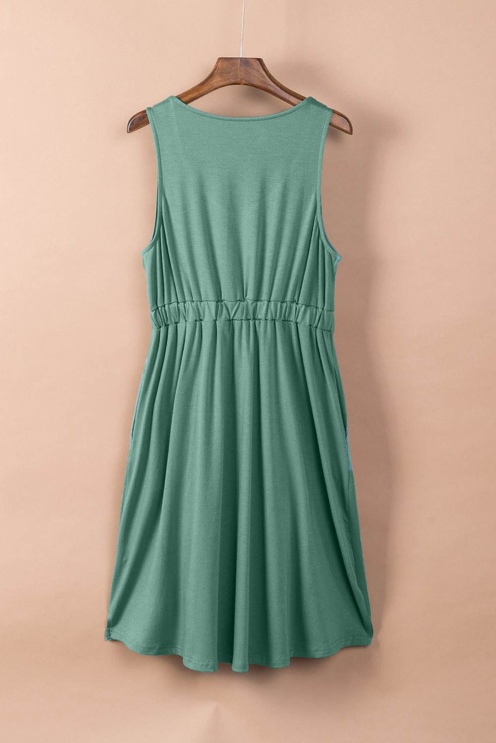 Elegant sage green sleeveless dress displayed on a wooden hanger against a neutral backdrop, featuring a gathered waist and a flowy skirt. Perfect for casual summer fashion.