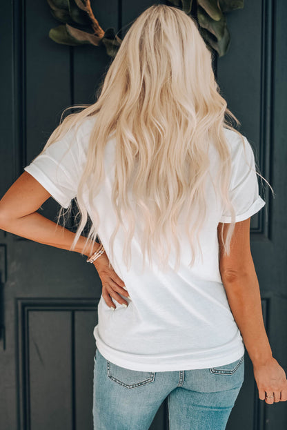 Blonde woman standing with back to the camera, featuring cascading waves, plain white tee, and fitted denim jeans, against a dark door with foliage. Elegant, casual style, perfect for fashion or hairstyle content.