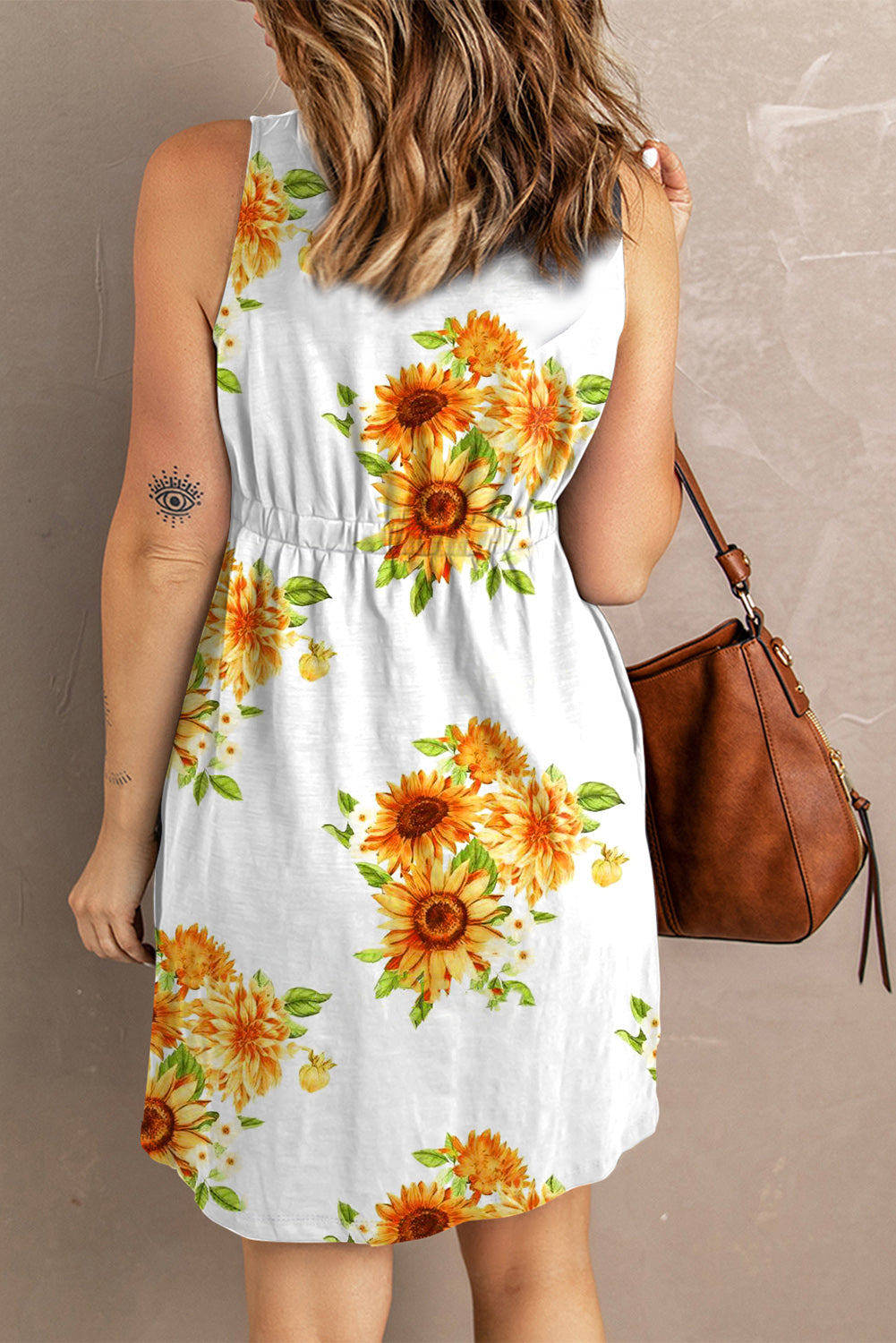 Woman in a floral sleeveless sundress with sunflower print, paired with a leather shoulder bag, showcasing a casual spring/summer fashion style.