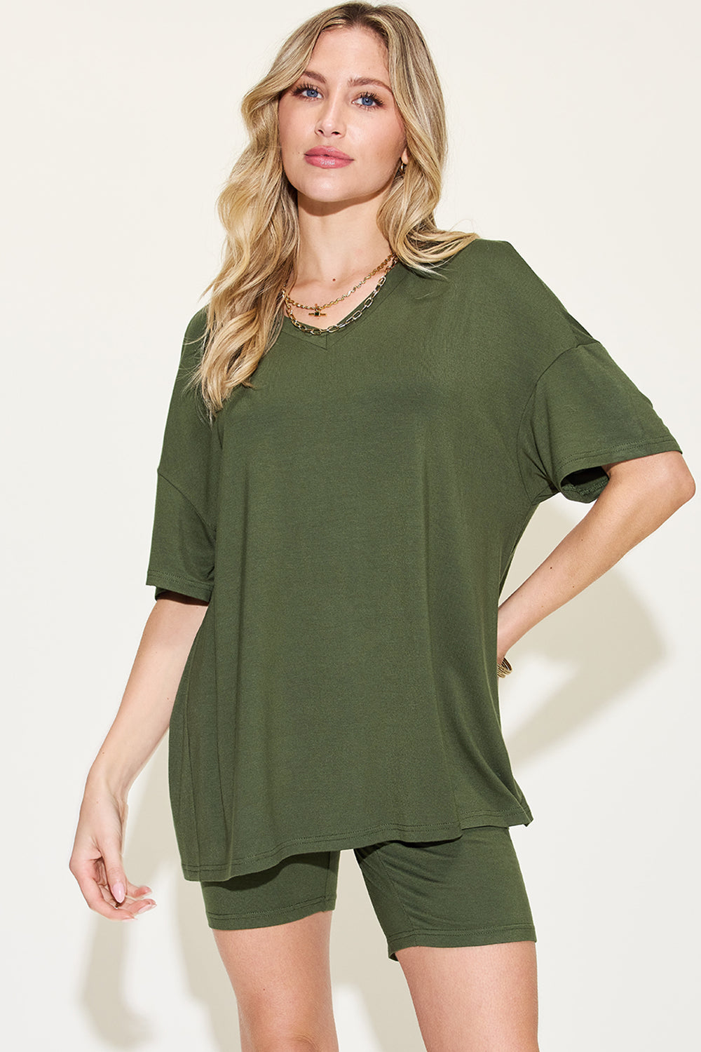 Chic woman models a casual olive green t-shirt and matching shorts, complemented by a layered chain necklace. Ideal for summer fashion trends.