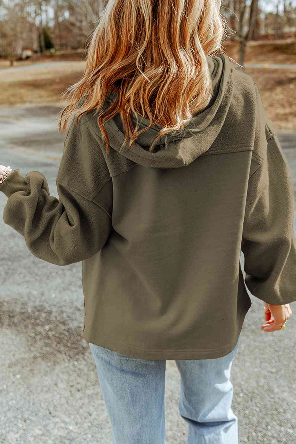 A woman from behind wearing a casual olive green hoodie and light-wash denim jeans, showcasing everyday autumn fashion outdoors.