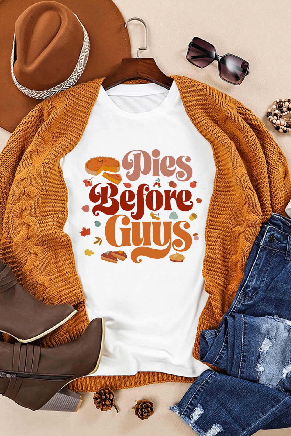 Autumn-themed fashion flat lay with a witty "Pies Before Guys" graphic tee, cozy mustard cardigan, distressed jeans, boots, hat, and accessories for a perfect casual fall look.