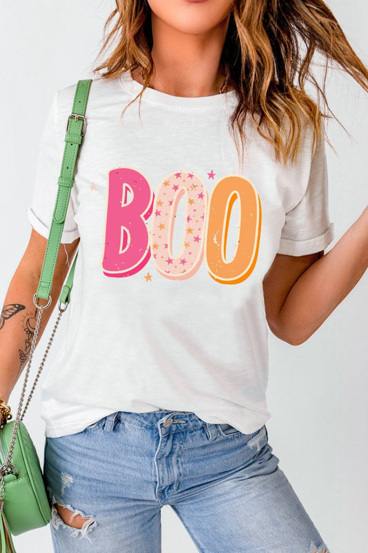 Stylish woman in a white tee with playful 'BOO' graphic, paired with distressed denim jeans and accessorized with a green crossbody bag. Perfect casual outfit for a fun, relaxed vibe.