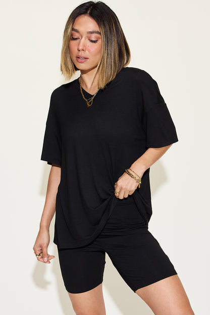 Casual chic woman models a trendy black oversized t-shirt and fitted cycling shorts, accessorized with gold jewelry, exuding effortless style. Perfect for summer fashion collections.