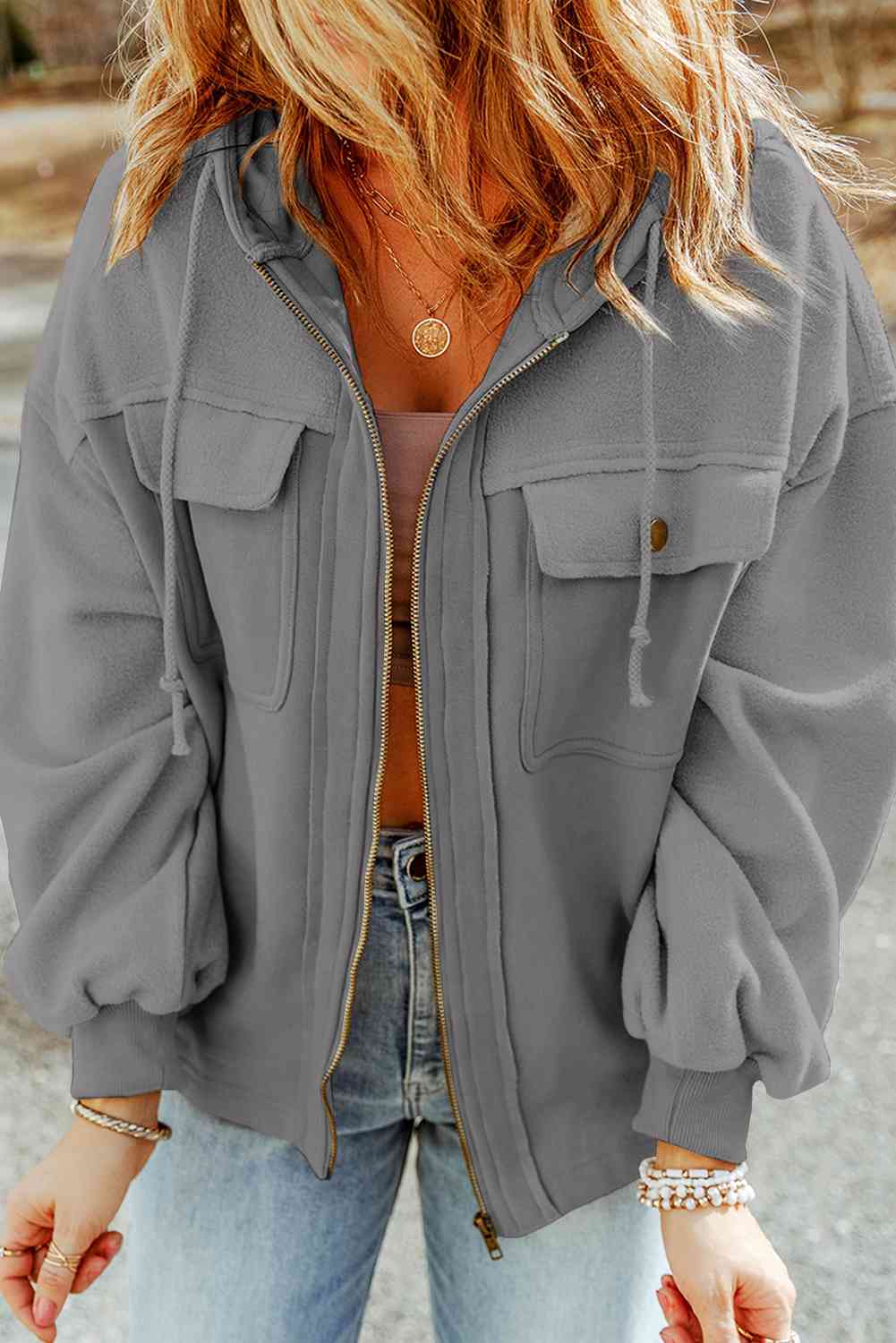 Woman in a casual gray jacket with zipper and pockets, paired with denim jeans and accessorized with simple jewelry, embodying a relaxed, everyday style. Perfect for a contemporary fashion blog or clothing retailer's social media.